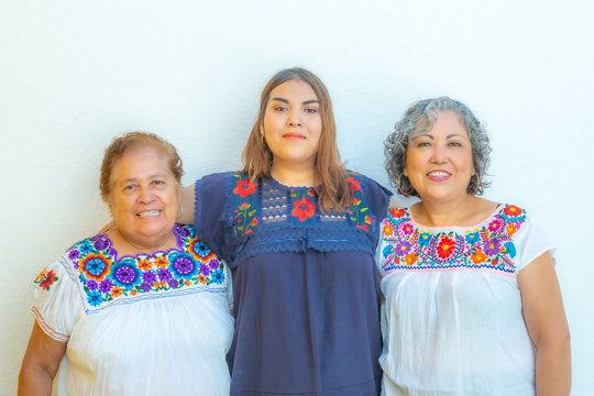 Three generations of latin Mexican women smiling in line, daughter, grandmother and granddaughter wearing casual clothes looking at the camera with a white background, space for text