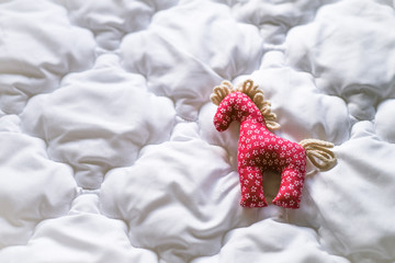 Country cottage home interior design detail background. Retro little red cotton fabric horse toy decoration lying on a white fluffy feather blanket.