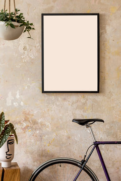 Modern composition of living room interior with black mock up poster frame,  wooden cube, flowers in vase, plant, hipster bike and personal accessories. Stylish home decor. Grunge wall. Template.