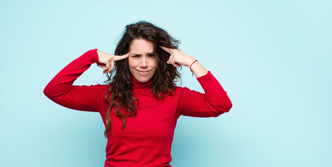 young pretty woman with a serious and concentrated look, brainstorming and thinking about a challenging problem against blue wall