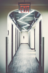 Emergency exit sign in empty corridor, selective focus, color toning applied. - obrazy, fototapety, plakaty