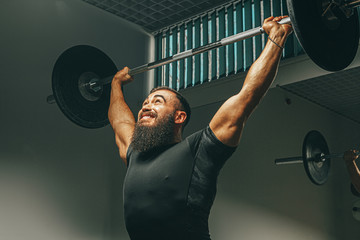 Muscular man in black sportswear lifting barbell in a gym