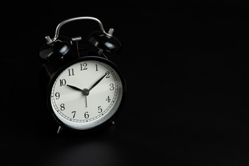 Black retro alarm clock in dark black bedroom with copy space using as sleeping time, clock of...