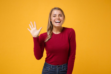 Obraz premium Cheerful young blonde woman girl in casual clothes posing isolated on yellow orange background in studio. People lifestyle concept. Mock up copy space. Waving greeting with hand as notices someone.