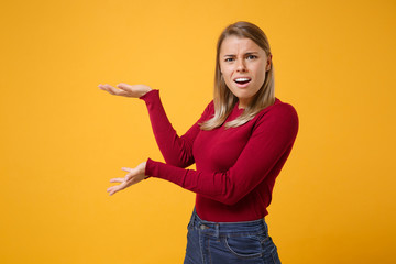 Bewildered perplexed young blonde woman girl in casual clothes posing isolated on yellow orange background studio portrait. People emotions lifestyle concept. Mock up copy space. Pointing hands aside.