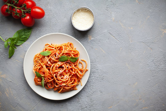 Tasty appetizing classic italian spaghetti pasta with tomato sauce, cheese parmesan and basil on plate on grey backgroound