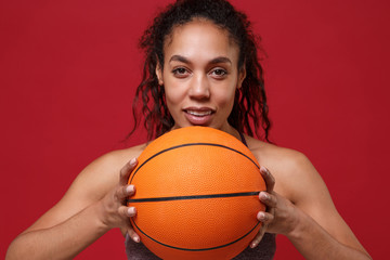 Close up of smiling african american sports fitness basketball player woman in sportswear working out isolated on red background. Sport exercises healthy lifestyle concept. Hold ball, looking aside.