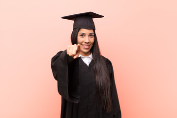 young latin woman student pointing at camera with a satisfied, confident, friendly smile, choosing...
