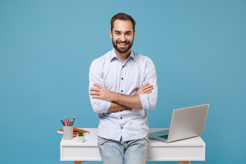 Smiling young bearded man in light shirt work near white desk with pc laptop isolated on pastel...