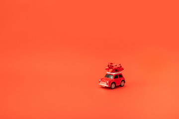 Holiday card or decor composition with red little toy car with a bow on a red background with...