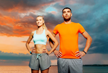 fitness, sport and people concept - happy couple exercising over sea and sunset sky on background