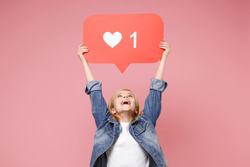Cheerful little kid girl 12-13 years old in denim jacket isolated on pastel pink background in studio. Childhood lifestyle concept. Mock up copy space. Hold huge like sign from Instagram heart form.