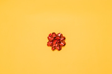Minimal composition of red shiny bow decor for a gift on a yellow background, top view