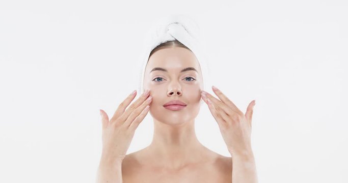 Young woman with blue eyes applying serum to her face, looking at camera, isolated on white background. Beautiful model girl with perfect clean fresh skin. Skin care treatment or cosmetic ads concept