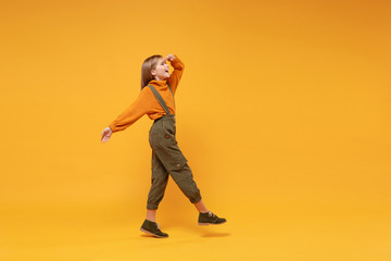 Side view of little kid girl 12-13 years old in turtleneck, jumpsuit isolated on yellow background. Childhood lifestyle concept. Mock up copy space. Holding hand at forehead looking far away distance.
