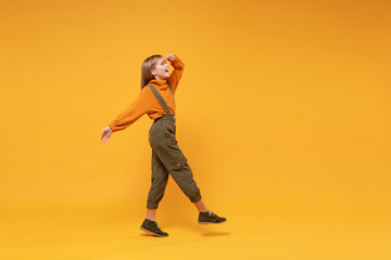 Side view of little kid girl 12-13 years old in turtleneck, jumpsuit isolated on yellow background....