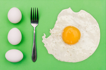 White eggs, fork and fried egg on a green background. Morning breakfast concept.