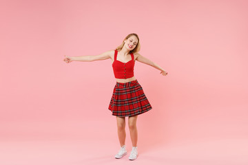 Cheerful young blonde woman girl in red sexy clothes isolated on pastel pink background studio portrait. People emotions lifestyle concept. Mock up copy space. Keeping eyes closed, spreading hands.