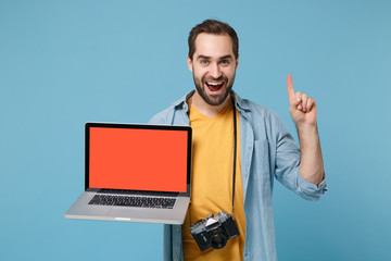 Traveler tourist man in casual clothes with photo camera isolated on blue background. Passenger traveling on weekends. Air flight journey. Hold laptop pc computer with empty screen, point finger up.