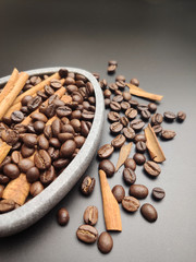 Scattered roasted coffee beans and a bowl of coffee and cinnamon on a black background close-up.