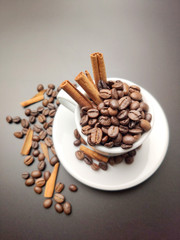 scattered coffee beans, a Cup with coffee beans and cinnamon sticks on a black background.
