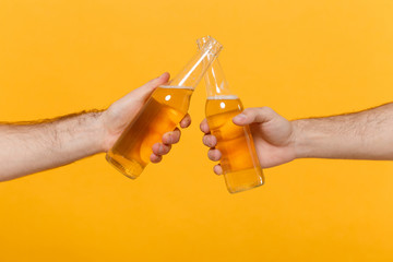 Close up cropped of two male hands horizontal holding lager beer glass bottles and clinking...