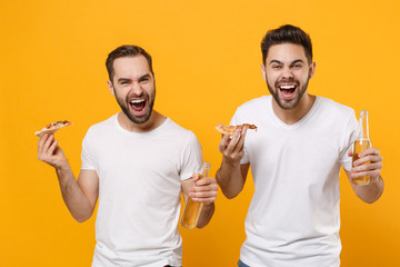 Laughing young men guys friends in white blank empty t-shirts posing isolated on yellow orange wall background. People emotions lifestyle concept. Mock up copy space. Hold beer bottles italian pizza.