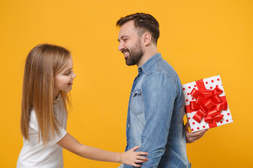 Obraz premium Side view of cheerful bearded man with child baby girl. Father little kid daughter isolated on yellow background. Love family day parenthood childhood concept. Hold present box with gift ribbon bow.
