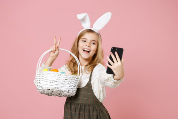 Little blonde kid girl 11-12 years old in spring dress bunny rabbit ears hold in hand cell phone...
