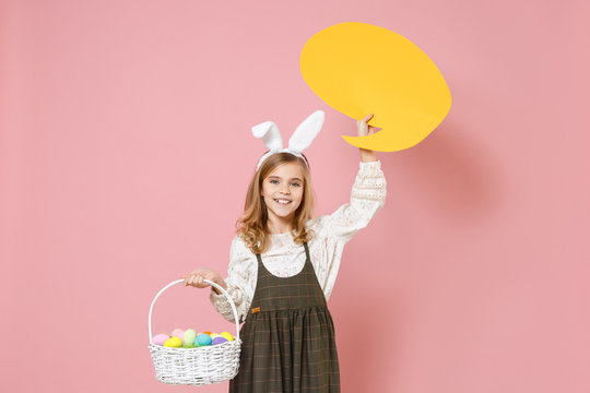Little pretty blonde kid girl 11-12 years old in spring dress, bunny rabbit ears hold in hand wicker basket colorful eggs Say cloud isolated on pastel pink background. Childhood Happy Easter concept.