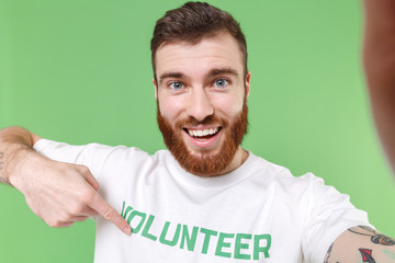Close up of excited young bearded man in white volunteer t-shirt isolated on green background....