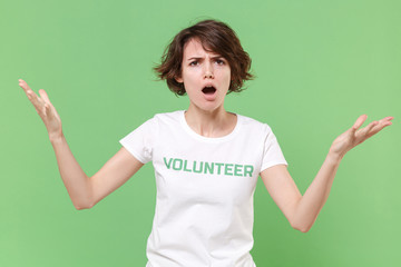 Irritated young brunette woman in white volunteer t-shirt isolated on pastel green background in...