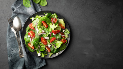 Healthy food. Top view of a fresh green vegetable salad of spinach, tomato, lettuce and sesame seeds on a plate. Black background. Copy space for text.