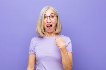senior or middle age pretty woman looking shocked and surprised with mouth wide open, pointing to...