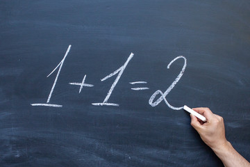 1 + 1=2 written with chalk on blackboard