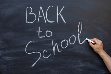 Chalkboard with back to school written in white chalk. The teacher writes on a chalkboard
