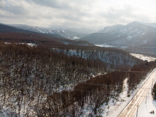 Fototapeta na wymiar Slopes of Tokiwa with trees and a road by the side of it with some vehicle for scale in Hokkaido during early winter with powerlines in photo 