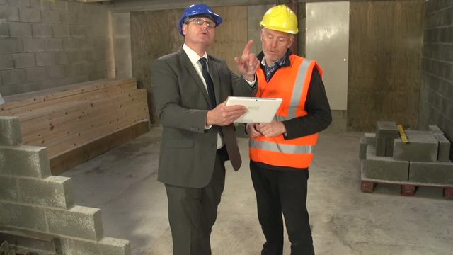 Two men wearing Hard Hats / Safety Helmets using a Digital Tablet on a construction / building site - Crane Shot - Stock Video Clip Footage