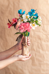 Unrecognizable woman hands holding a beautiful bouquet of colorful spring flowers against crafty brown paper background