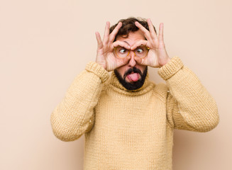 young cool man smiling happily with funny face, joking and looking through peephole, spying on...