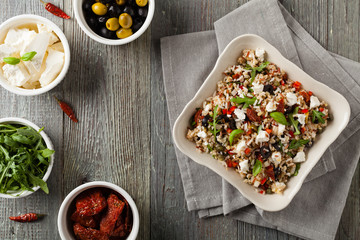 Trendy lunch with red rice, a mix of groats and vegetables. Top view. Served in white bowl on grey wooden background.