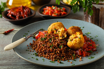 Lentil and millet meatballs. Served on tomato salsa with buckwheat. Gray plate, wooden boards in the background. Front view.