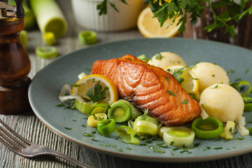 Portion of fried salmon, served with mashed potatoes and cooked leek. Front view. Gray plate, wooden background.