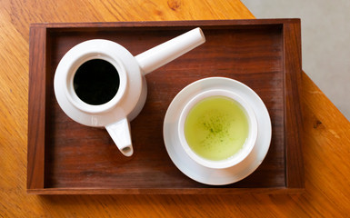 Japanese green tea in white cup and teapot on dark wooden serving tray on table, top view. Cafe, life style