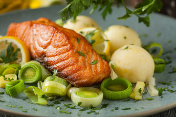 Portion of fried salmon, served with mashed potatoes and cooked leek. Front view. Gray plate, wooden background.