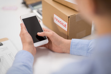 delivery, mail service, people and shipment concept - close up of woman's hands with smartphone and parcel boxes at post office