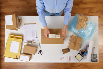 delivery, mail service, people and shipment concept - close up of woman packing parcel box with adhesive tape at post office