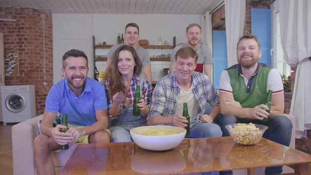 Group of friends watching tv at home drinking beer and discussing