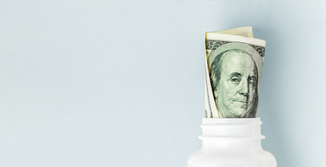 Money Bills in white pill bottle on blue background. medical concept with copyspace