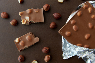 sweets, confectionery and food concept - milk chocolate bar with hazelnuts in foil wrapper on brown background